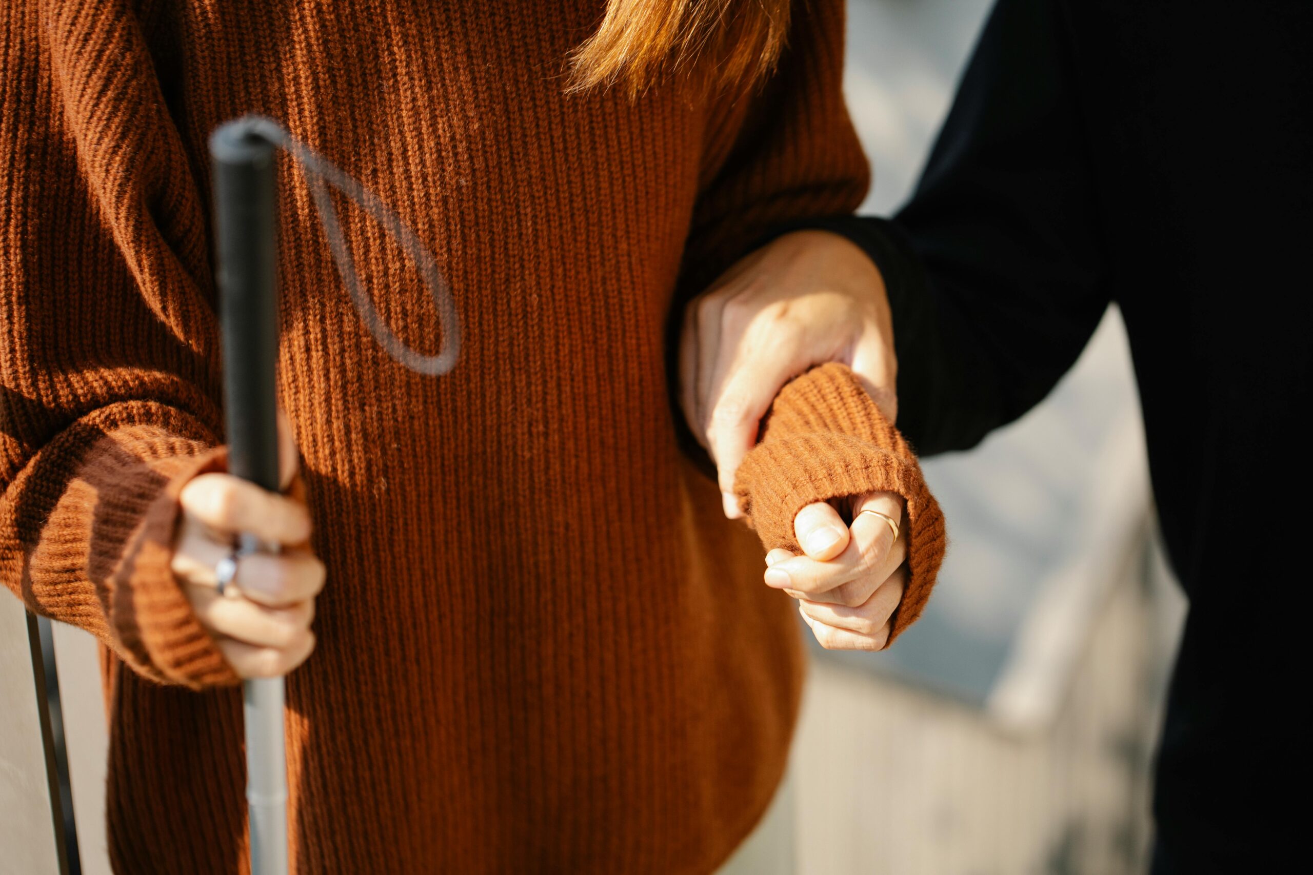 Close-up of two people holding hands, one with a walking cane symbolizing support and visual aid.