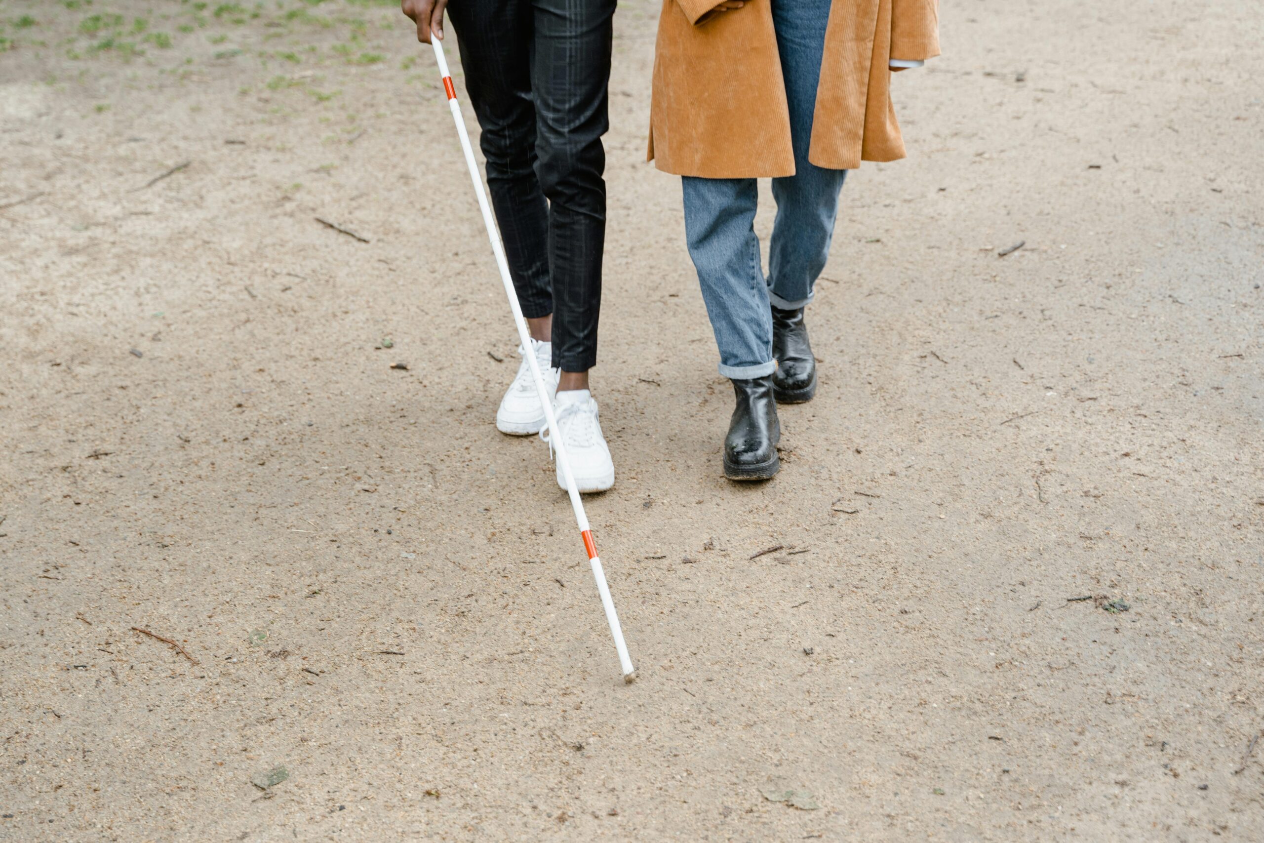 Two people walking on a path, one using a white cane for visually impaired assistance.