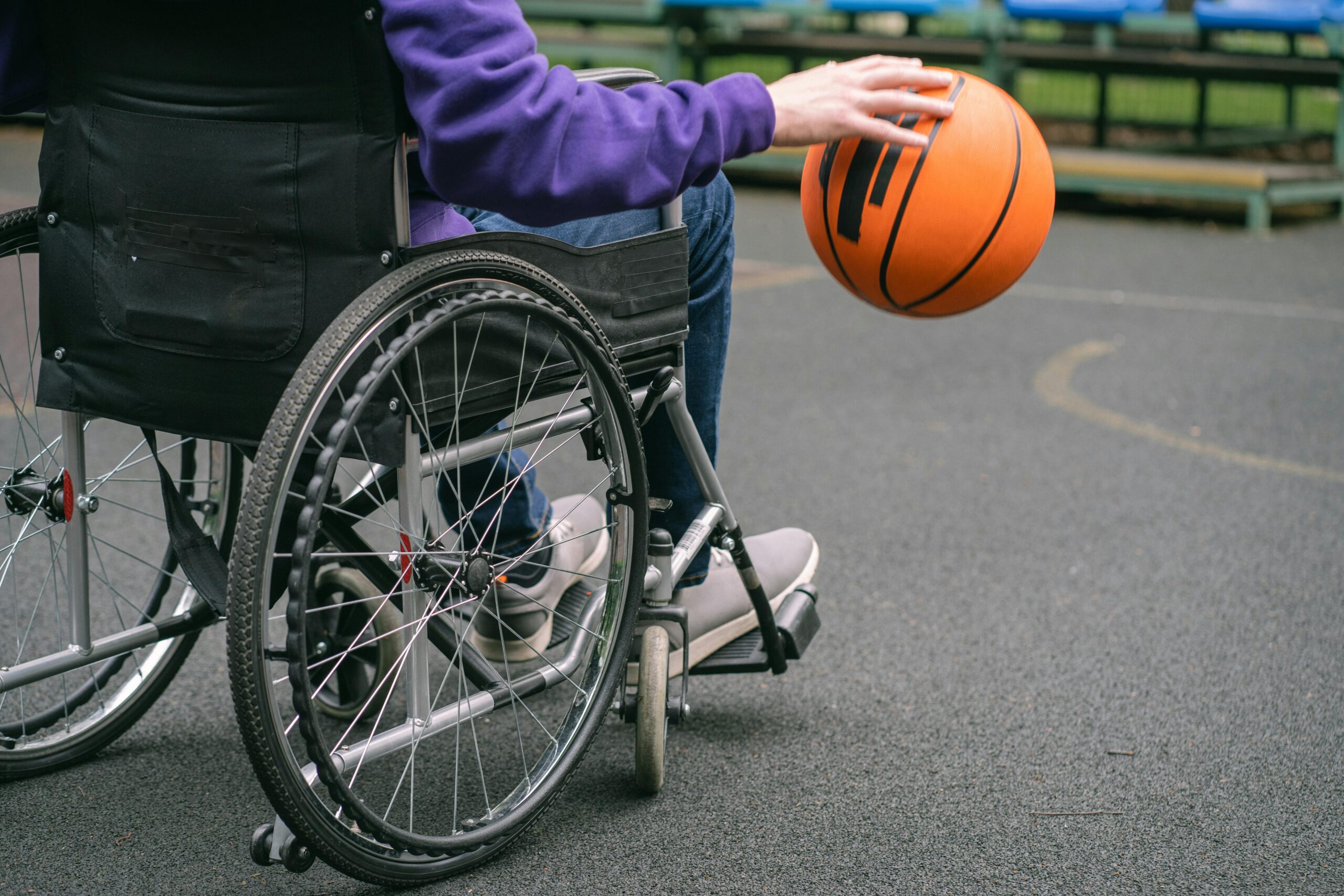 Close-up of a person in a wheelchair playing basketball outdoors, highlighting inclusivity and sports spirit.